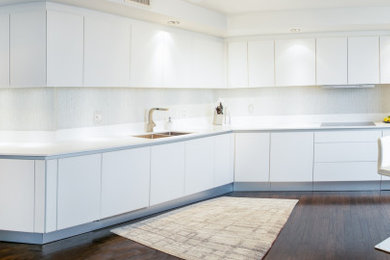 Inspiration for a mid-sized contemporary single-wall dark wood floor and brown floor enclosed kitchen remodel with a double-bowl sink, glass-front cabinets, white cabinets, quartz countertops, white backsplash, glass tile backsplash, stainless steel appliances, a peninsula and white countertops