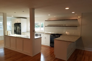 Example of a mid-sized transitional l-shaped medium tone wood floor and brown floor open concept kitchen design in Other with an undermount sink, recessed-panel cabinets, white cabinets, granite countertops, white backsplash, subway tile backsplash, black appliances, an island and beige countertops