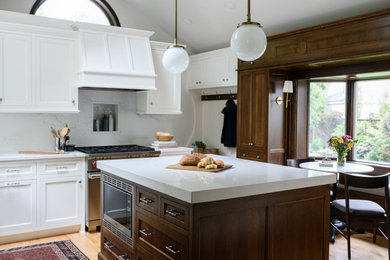 Mid-sized elegant l-shaped light wood floor and vaulted ceiling enclosed kitchen photo in Minneapolis with a single-bowl sink, recessed-panel cabinets, white cabinets, quartz countertops, white backsplash, quartz backsplash, stainless steel appliances, an island and white countertops
