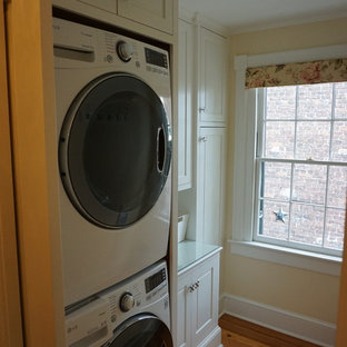 Photo of a small traditional galley separated utility room in DC Metro with white cabinets, glass worktops, beige walls, dark hardwood flooring, a stacked washer and dryer and raised-panel cabinets.