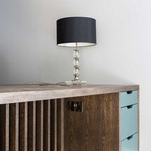 他の地域の大きいモダンスタイルのおしゃれな書斎 (グレーの壁、無垢フローリング、標準型暖炉、木材の暖炉まわり、造り付け机、茶色い床) の写真