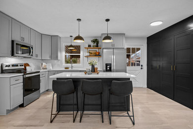 Example of a mid-sized trendy l-shaped laminate floor and brown floor open concept kitchen design in Nashville with an undermount sink, shaker cabinets, gray cabinets, quartz countertops, white backsplash, ceramic backsplash, stainless steel appliances, an island and white countertops