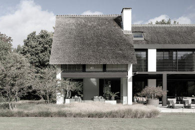 Example of a large minimalist white two-story stucco exterior home design in Amsterdam with a mixed material roof and a brown roof