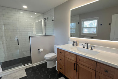 Example of a mid-sized minimalist master white tile and subway tile porcelain tile, black floor and single-sink alcove shower design in Indianapolis with shaker cabinets, light wood cabinets, a two-piece toilet, gray walls, an integrated sink, quartz countertops, a hinged shower door, white countertops, a niche and a freestanding vanity