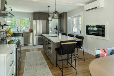 Large trendy l-shaped medium tone wood floor kitchen photo in Boston with an undermount sink, shaker cabinets, gray cabinets, quartz countertops, gray backsplash, ceramic backsplash, stainless steel appliances, an island and white countertops
