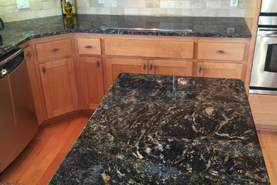 Example of a mid-sized classic l-shaped medium tone wood floor and brown floor kitchen design in Minneapolis with shaker cabinets, medium tone wood cabinets, granite countertops, beige backsplash, stone tile backsplash, stainless steel appliances and an island