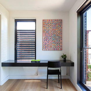 Photo of a mid-sized contemporary home office in Melbourne with a library, white walls, light hardwood floors, a built-in desk and beige floor.