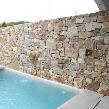 detalle de muro de piedra natural frente a piscina con cascada integrada y grifo