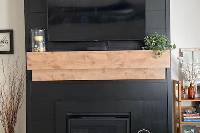 Small farmhouse laminate floor living room photo in Other with black walls, a shiplap fireplace and a wall-mounted tv