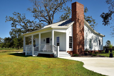 Photo of a small country one-storey white house exterior with concrete fiberboard siding, a gable roof and a metal roof.