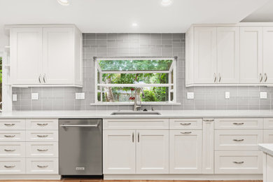 Large trendy l-shaped medium tone wood floor, brown floor and vaulted ceiling eat-in kitchen photo in Seattle with an undermount sink, shaker cabinets, white cabinets, quartz countertops, gray backsplash, glass tile backsplash, stainless steel appliances, an island and gray countertops