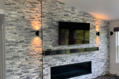 Living room - large contemporary vinyl floor and gray floor living room idea in Portland with gray walls, a standard fireplace, a stacked stone fireplace and a wall-mounted tv