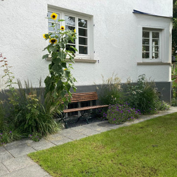 Eine Bank vor dem Haus umrahmt von Stauden.