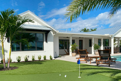 Example of a mid-sized beach style white one-story stucco and board and batten exterior home design in Miami with a metal roof and a gray roof
