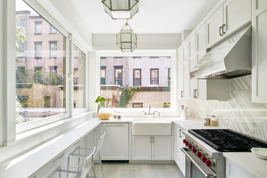 Example of a transitional l-shaped gray floor enclosed kitchen design in New York with a farmhouse sink, shaker cabinets, white cabinets, gray backsplash, stainless steel appliances, no island and white countertops