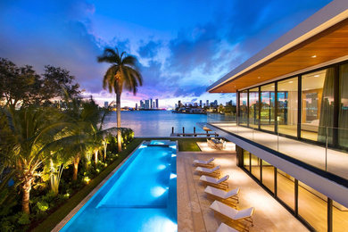Photo of a large contemporary backyard rectangular infinity pool in Miami with a hot tub and natural stone pavers.