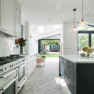 Classic galley kitchen in London with shaker cabinets, grey cabinets, white splashback, stainless steel appliances, light hardwood flooring, an island, grey floors and white worktops.