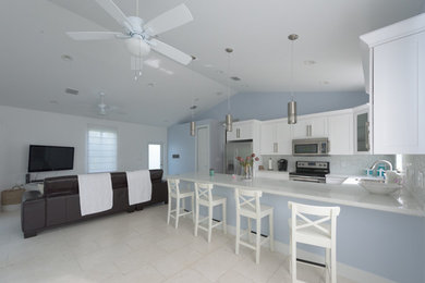 Mid-sized beach style u-shaped ceramic tile eat-in kitchen photo in Miami with a drop-in sink, shaker cabinets, white cabinets, solid surface countertops, multicolored backsplash, mosaic tile backsplash, stainless steel appliances and a peninsula