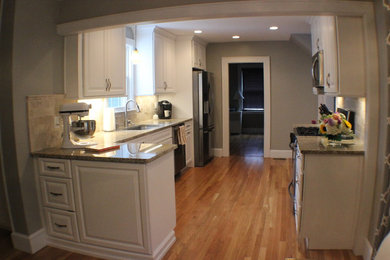 Photo of a mid-sized traditional l-shaped eat-in kitchen in Boston with an undermount sink, raised-panel cabinets, white cabinets, granite benchtops, beige splashback, marble splashback, stainless steel appliances and light hardwood floors.