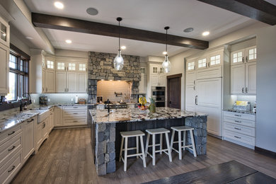 Example of a large cottage u-shaped medium tone wood floor, brown floor and exposed beam eat-in kitchen design in Edmonton with a farmhouse sink, raised-panel cabinets, white cabinets, granite countertops, green backsplash, glass tile backsplash, paneled appliances, an island and multicolored countertops