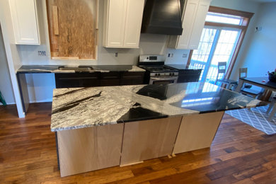 Large minimalist single-wall dark wood floor and brown floor eat-in kitchen photo in Bridgeport with an undermount sink, black cabinets, granite countertops, stainless steel appliances, an island and black countertops