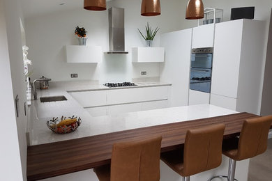 Inspiration for a medium sized contemporary u-shaped kitchen/diner in Hertfordshire with a single-bowl sink, flat-panel cabinets, white cabinets, quartz worktops, white splashback, stainless steel appliances, ceramic flooring, a breakfast bar and beige floors.