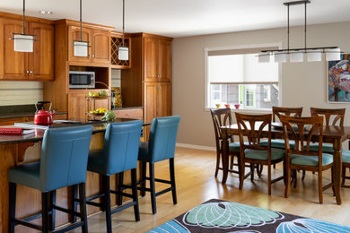 Example of a large eclectic l-shaped light wood floor and beige floor eat-in kitchen design in Seattle with an undermount sink, raised-panel cabinets, medium tone wood cabinets, granite countertops, white backsplash, ceramic backsplash, stainless steel appliances, an island and brown countertops