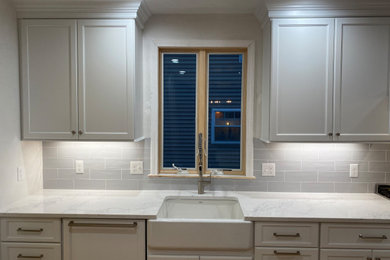 Large elegant single-wall light wood floor and beige floor eat-in kitchen photo in Boston with a farmhouse sink, shaker cabinets, white cabinets, quartz countertops, gray backsplash, ceramic backsplash, stainless steel appliances, an island and white countertops