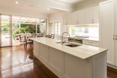 This is an example of a mid-sized traditional galley eat-in kitchen in Brisbane with a drop-in sink, beaded inset cabinets, white cabinets, limestone benchtops, white splashback, stainless steel appliances, medium hardwood floors, with island and white benchtop.