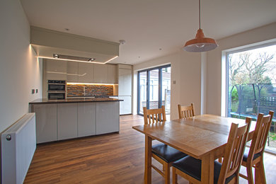 Photo of a mid-sized contemporary single-wall eat-in kitchen in Surrey with an integrated sink, flat-panel cabinets, beige cabinets, quartzite benchtops, multi-coloured splashback, stone tile splashback, panelled appliances, vinyl floors, with island and black benchtop.