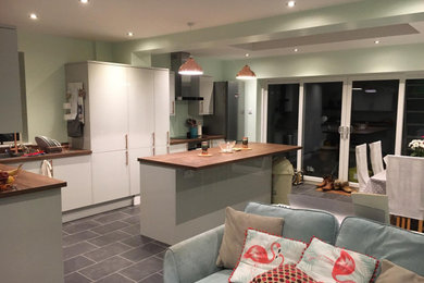 This is an example of a medium sized contemporary galley open plan kitchen in Devon with flat-panel cabinets, white cabinets, wood worktops, ceramic flooring, an island, grey floors and brown worktops.