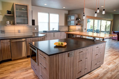 Mid-sized trendy l-shaped porcelain tile and gray floor open concept kitchen photo in Other with an undermount sink, gray cabinets, granite countertops, gray backsplash, glass tile backsplash, stainless steel appliances and an island
