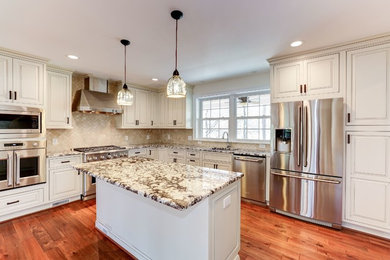 This is an example of a mid-sized traditional u-shaped open plan kitchen in DC Metro with an undermount sink, raised-panel cabinets, white cabinets, granite benchtops, beige splashback, mosaic tile splashback, stainless steel appliances, dark hardwood floors, with island, brown floor and beige benchtop.