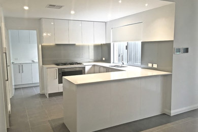 Contemporary u-shaped eat-in kitchen in Perth with a double-bowl sink, flat-panel cabinets, white cabinets, quartz benchtops, metallic splashback, glass sheet splashback, stainless steel appliances, ceramic floors and with island.