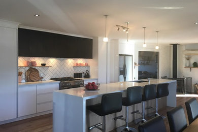 Photo of a large contemporary galley open plan kitchen in Other with an undermount sink, flat-panel cabinets, white cabinets, quartz benchtops, white splashback, ceramic splashback, stainless steel appliances, light hardwood floors and with island.