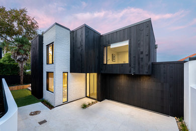 Photo of a mid-sized contemporary two-storey black exterior in Auckland with wood siding, a flat roof, a metal roof and a black roof.