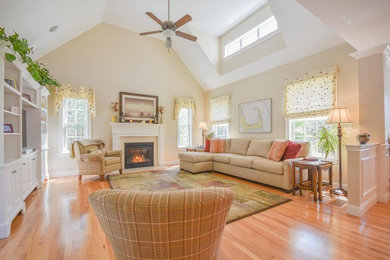 Photo of a mid-sized traditional open concept family room in Boston with beige walls, light hardwood floors, a standard fireplace, a wood fireplace surround, a built-in media wall and brown floor.