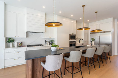 Trendy l-shaped medium tone wood floor and brown floor kitchen photo in Calgary with an undermount sink, shaker cabinets, white cabinets, white backsplash, stone slab backsplash, stainless steel appliances, an island and white countertops