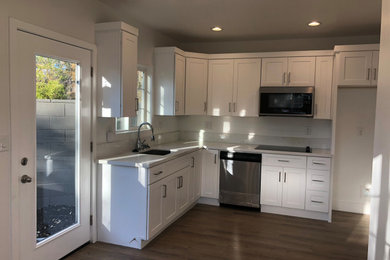 Photo of a mid-sized traditional l-shaped open plan kitchen in Los Angeles with an undermount sink, shaker cabinets, white cabinets, quartzite benchtops, beige splashback, stone slab splashback, stainless steel appliances, vinyl floors, no island, brown floor, beige benchtop and recessed.