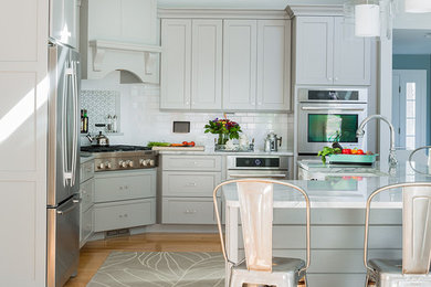 This is an example of a mid-sized transitional l-shaped open plan kitchen in Boston with a farmhouse sink, flat-panel cabinets, grey cabinets, quartzite benchtops, white splashback, subway tile splashback, stainless steel appliances, light hardwood floors and with island.