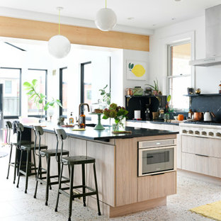 Diseño de cocina retro, abierta, con armarios con paneles lisos, puertas de armario de madera clara, encimera de mármol, salpicadero negro, salpicadero de mármol, electrodomésticos de acero inoxidable, suelo de terrazo y una isla