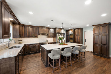 Example of a large l-shaped dark wood floor and brown floor kitchen pantry design in Detroit with a single-bowl sink, raised-panel cabinets, dark wood cabinets, quartz countertops, beige backsplash, ceramic backsplash, stainless steel appliances, an island and beige countertops