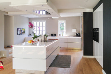 Inspiration for a large contemporary open plan kitchen in Hamburg with an undermount sink, white cabinets, quartzite benchtops, black appliances, light hardwood floors, with island and white splashback.