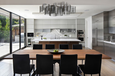 Mid-sized contemporary l-shaped eat-in kitchen in San Francisco with an undermount sink, flat-panel cabinets, grey cabinets, quartz benchtops, white splashback, marble splashback, stainless steel appliances, light hardwood floors, with island and white benchtop.