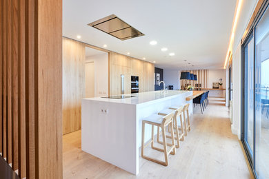 Imagen de cocina comedor alargada actual grande con fregadero integrado, armarios con paneles lisos, puertas de armario de madera oscura, encimera de cuarzo compacto, electrodomésticos negros, suelo de madera en tonos medios, una isla y suelo beige