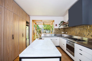 Photo of a mid-sized contemporary u-shaped open plan kitchen in Melbourne with a double-bowl sink, flat-panel cabinets, white cabinets, stainless steel benchtops, green splashback, ceramic splashback, stainless steel appliances, medium hardwood floors and with island.