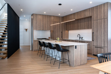 Trendy l-shaped laminate floor and brown floor eat-in kitchen photo in Other with an undermount sink, flat-panel cabinets, medium tone wood cabinets, quartz countertops, white backsplash, quartz backsplash, paneled appliances, an island and white countertops