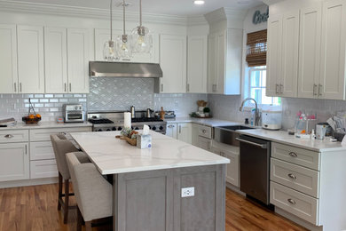 Mid-sized transitional l-shaped light wood floor and brown floor eat-in kitchen photo in Other with a farmhouse sink, shaker cabinets, white cabinets, quartz countertops, white backsplash, subway tile backsplash, stainless steel appliances, an island and multicolored countertops