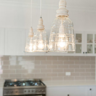 Idée de décoration pour une grande arrière-cuisine champêtre en L avec un évier encastré, des portes de placard blanches, une crédence beige, une crédence en carreau de terre cuite, un électroménager en acier inoxydable et un îlot central.