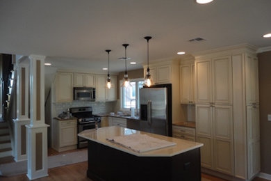 Kitchen - transitional l-shaped medium tone wood floor kitchen idea in New York with distressed cabinets, granite countertops, beige backsplash, ceramic backsplash, stainless steel appliances and an island